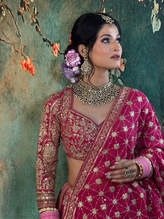 Bride in magenta and gold, kundan choker, hair pinned with fresh flowers