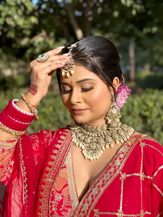Bride in a scarlet and gold saree adjusting her maang tikka